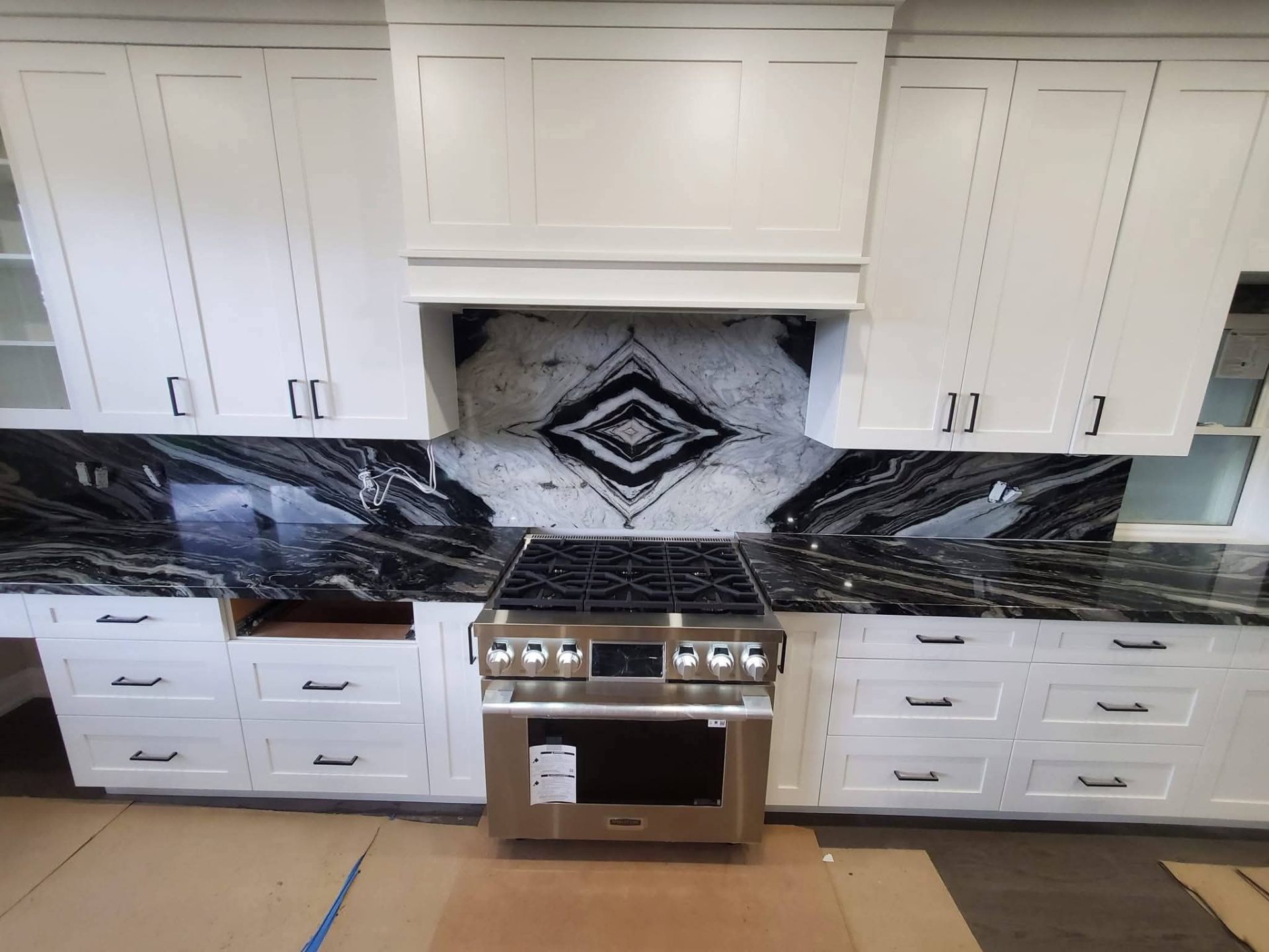 Black granite countertops and bookmatched dramatic veined slab backsplash with white shaker cabinets and stainless range — Seattle area kitchen