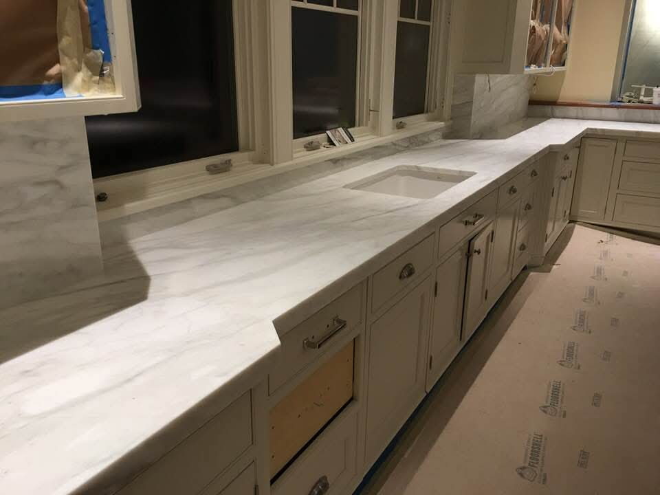 White marble kitchen countertop with undermount sink, cream cabinets and bay windows