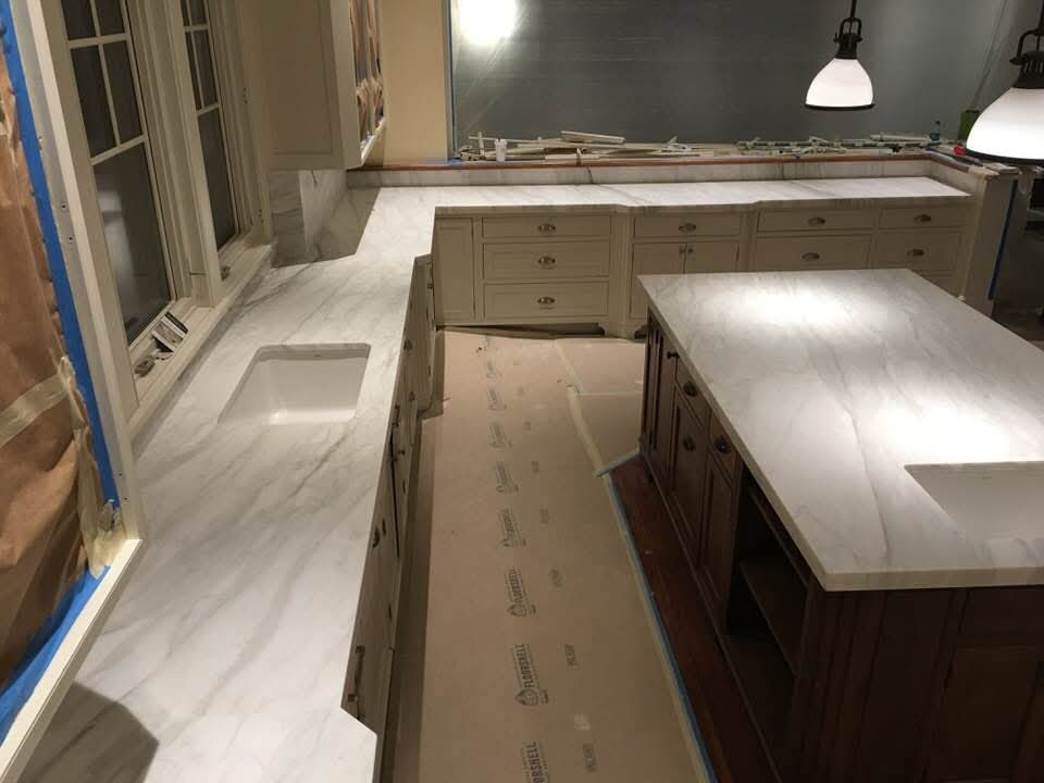 White marble U-shaped kitchen and island countertops mid-installation with cream cabinets
