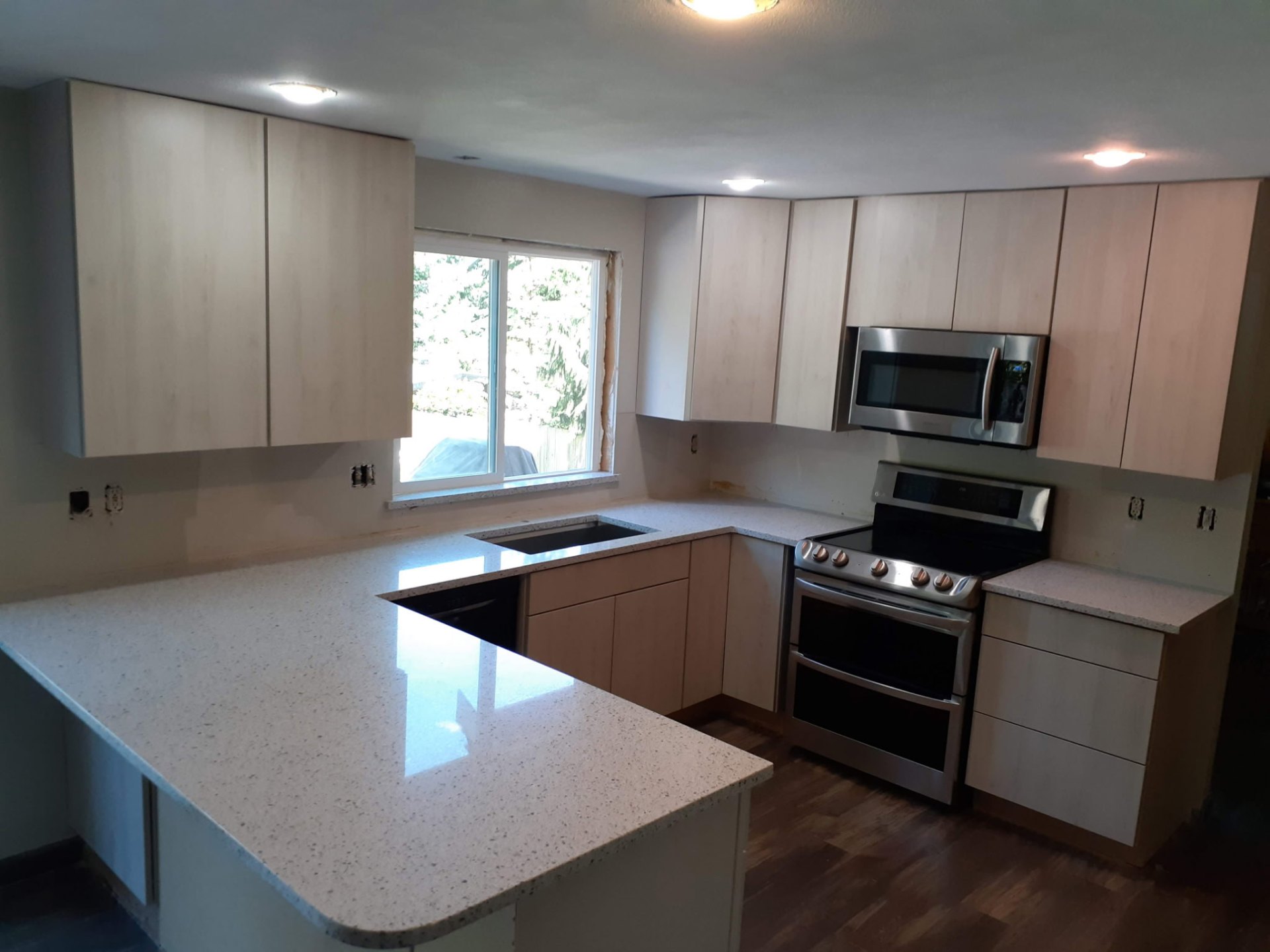 White speckled quartz U-shaped kitchen countertop with light wood cabinets and stainless appliances
